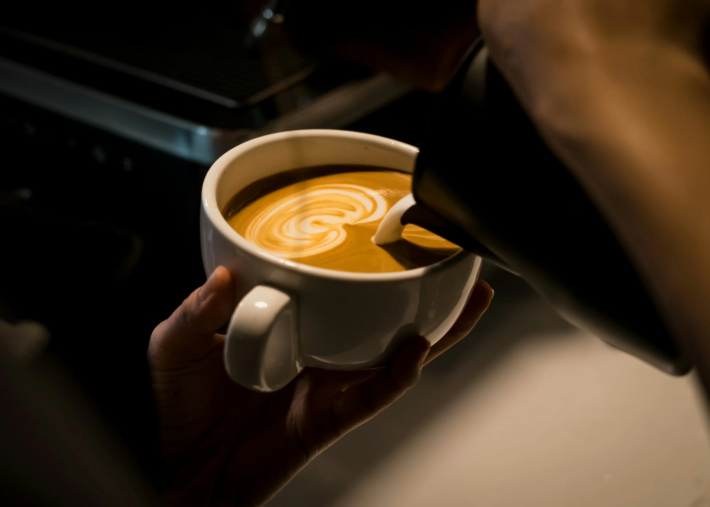 A barista pouring a curved latte-art pattern into a white ceramic cup